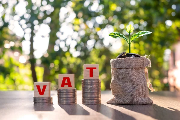 Wooden block with vat text on stacked coins and tree on tong vat concept VAT charged by the government on the purchase of goods or services.