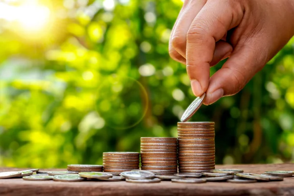 Mali büyüme ve yatırım konsepti için büyüyen bir yığına madeni para koyan bir insan elinin yakın çekimi: iş zenginliği yönetimi, uzun vadeli tasarruf stratejisi ve bulanık yeşil arka planlı sürdürülebilir bankacılık.