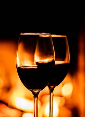 Şömine ışığının arka planında iki kadeh kırmızı şarap. Noel tatili kavramı