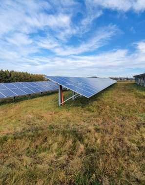 Bulutlu mavi gökyüzü olan bir çayırdaki güneş hücreleri. Güneş panelleri, fotovoltaik, alternatif enerji kaynağı. Sürdürülebilir kaynaklar kavramı.