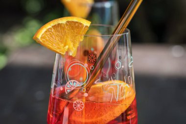 Renkli portakallı aperatif içeceğe yakın plan portakal dilimi ve dekoratif bardakta şeffaf bir kamış. Yumuşak arkaplanlı parlak yaz içeceği. Bar kültürü, parti, yaşam tarzı, ferahlatıcı ve sıcak akşamlar kavramı.
