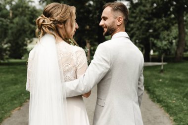 Gelin ve damat el ele tutuşun ve arkanıza bakın, şık bir düğün çifti parkta yürüyüş için, gelin ve damat kameraya dönük, genç bir çiftin düğün günü