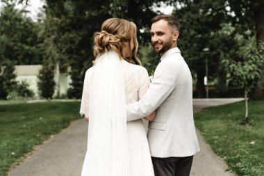 Gelin ve damat el ele tutuşun ve arkanıza bakın, şık bir düğün çifti parkta yürüyüş için, gelin ve damat kameraya dönük, genç bir çiftin düğün günü