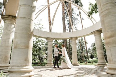 Yeşil bir parkta kucaklaşan ve gülümseyen yeni evliler. Dantel bir elbise içinde gelin ve damadın portresi. Yeni evli çiftin düğün günü.