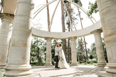 Yeşil bir parkta kucaklaşan ve gülümseyen yeni evliler. Dantel bir elbise içinde gelin ve damadın portresi. Yeni evli çiftin düğün günü.