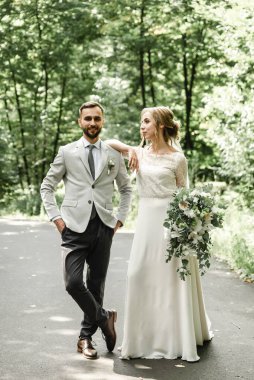 Yeşil bir parkta kucaklaşan ve gülümseyen yeni evliler. Dantel bir elbise içinde gelin ve damadın portresi. Yeni evli çiftin düğün günü.