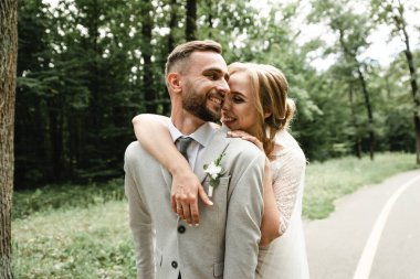 Gelin, damada nazikçe arkadan sarılır ve kulağına düğün günü güzel sözler fısıldar, düğün çifti. Düğün buketi olan mutlu gelin damadın kolunu tutuyor. Yeni evli, şık bir çift. Evlilik kavramı. Kırsal düğün