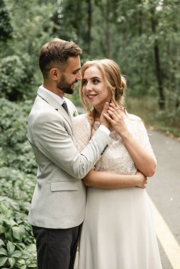 Tatil yeni evliler, genç bir çiftin şefkatli kucaklaşmaları, damat gelinin yüzüne dokunuyor, neşeli ve neşeli düğün çifti parkta yürüyor.