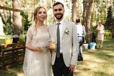 Gelin ve damat, doğadaki misafirler çemberinde içkilerinin tadını çıkarırlar. Gelin ve damat, bahçede misafirlerle birlikte bir içkinin tadını çıkarırlar. Aşık bir çiftin düğün günü.