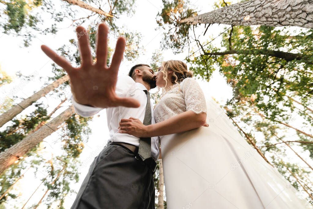 the groom and the bride kiss the view from below, the groom's hand in the foreground,creative wedding photography,happy wedding day in nature