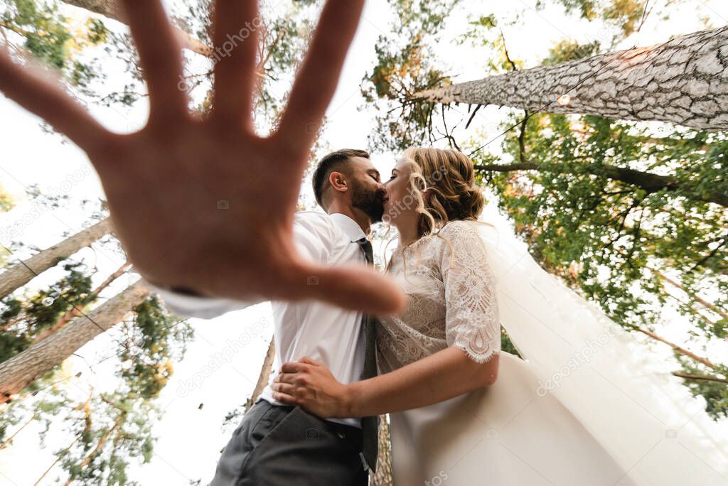 the groom and the bride kiss the view from below, the groom's hand in the foreground,creative wedding photography,happy wedding day in nature