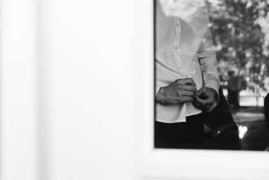 Beyaz gömlekli genç adam evde düğmesini ilikliyor. Damat toplanıyor. Damat evde. Adam giyiniyor. Kendini izole eden adam pencereden bakar.