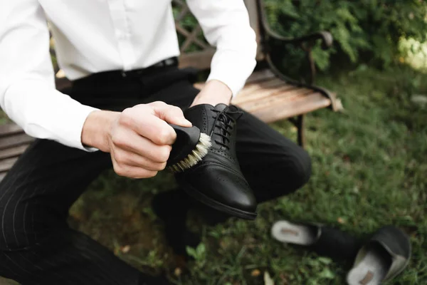 a man cleans leather men\'s shoes with a brush and a rag. black shoes with a tassel. leather shoes on the table with polishing equipment. shoe shine, fashion, handicraft.