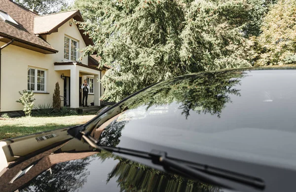 Takım elbiseli bir adam ve üzerinde klasik bir yelek bulunan bir gömlek evinin yanında duruyor. Uşak. Hizmetçiler. Genç damadın şık kıyafetleri.