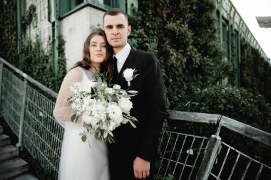 Zengin damat ve gelin, sarmaşıkla kaplı parkta güzel güzel yürüyorlar. Genç bir ailenin düğün günü. Yeni evliler. Evliliğin başlangıcı. Güçlü bir aile. romantik ilişki