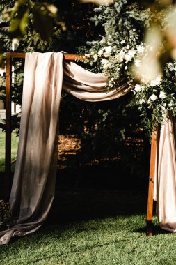 Kahverengi ipek kumaş güllerle süslenmiş ahşap bir düğün sunağında asılı. Düğün süsleri. Çiçekçilik. Düğün kemeri. Misafirler için fotoğraf alanı, düğün dekoru