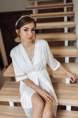 Gelinlik giymiş güzel bir gelin beyaz önlüklü beyaz bir duvarın karşısında duruyor. Gelinin ücreti. Bekârlığa veda partisi. düğün günü.