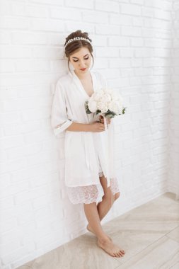 Gelinlik giymiş güzel bir gelin beyaz önlüklü beyaz bir duvarın karşısında duruyor. Gelinin ücreti. Bekârlığa veda partisi. düğün günü.