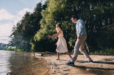 Mutlu genç bir çift göl kenarında el ele koşup suya taş atıyor. Doğada bir erkekle güzel bir kız yürüyor. romantik randevu