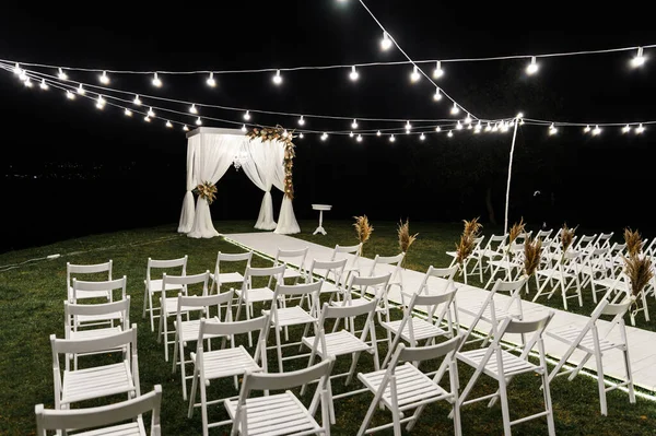 beautiful night stage for the wedding ceremony. wedding wooden arch. stylish wedding decor. chairs for the wedding ceremony. decorative bulbs illuminate the site. empty wedding venue