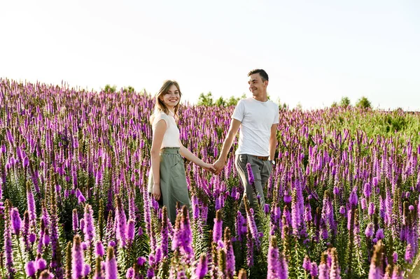 春の花が咲く野原の夕焼けの中を素敵なカップルが歩いています 春のロマンチックな散歩 あの日の日没時の幸せなカップル — ストック写真