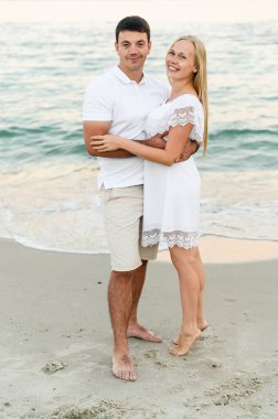 Mutlu çift gün batımında deniz kıyısında sarılıyor. Aşıkların yaz aşkı. Denize doğru yürü. Balayına çıkmış yeni evliler. Romantik zamanlar. Mutlu gençler..