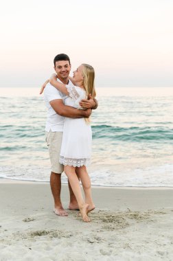 Okyanus kenarındaki aşıklar sarılıp eğleniyorlar. Karı koca gün batımında deniz kenarında kucaklaşır. Tatildeki aşıklar. Yaz tatili. Okyanusta romantik bir yürüyüş.