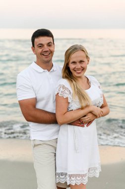 Okyanus kıyısında sahilde yürürken bir erkekle kucaklaşan mutlu bir kız. Romantik yürüyüş. Karı koca deniz kenarında gülüp sarılıyor. Yaz tatili. Genç bir çiftin tatili.