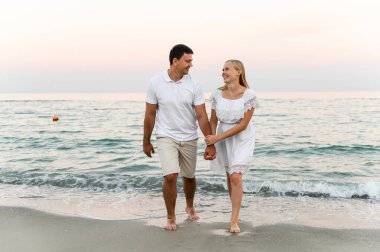 Okyanus kenarındaki aşıklar sarılıp eğleniyorlar. Karı koca gün batımında deniz kenarında kucaklaşır. Tatildeki aşıklar. Yaz tatili. Okyanusta romantik bir yürüyüş.