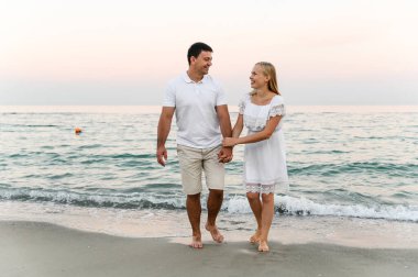 Okyanus kenarındaki aşıklar sarılıp eğleniyorlar. Karı koca gün batımında deniz kenarında kucaklaşır. Tatildeki aşıklar. Yaz tatili. Okyanusta romantik bir yürüyüş.