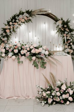 Düğün süslemeleriyle süslenmiş yeni evliler için güzel bir ziyafet masası. Gelin ve damat için yemek masası. Ahşap kemer, masada çiçeklerle süslenir..