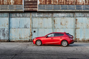 Eski bir uçak hangarının önüne park edilmiş kırmızı bir Mazda 3. Mazda 3 2013-2019 'da üretildi. Katowice - Polonya, 15 Şubat 2015