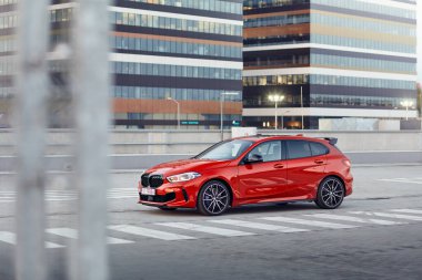 Kırmızı BMW M135i ofis binalarının önündeki otoparkta. Model F40, 2019 'dan üretildi. 306 hp motor, ivme 0-100 km / saat: 4.8 s. Katowice, Polonya - 16 Eylül 2020