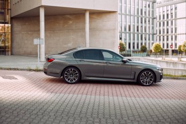 Lüks gri BMW 740 D, modern bir ofis binasının yanına park edilmiş. Başka araba ve insanlar yok. Katowice, Polonya, 12.06.2021