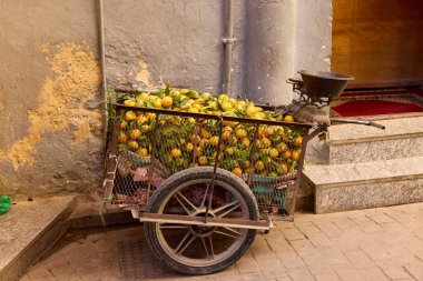 Fas 'ta bir kaldırım taşı caddesinde içi taze meyve dolu bir araba duruyor. Sıcak öğle güneşi ürünlerin canlı renklerini vurguluyor ve yerel pazar kültürünün özünü yakalıyor.