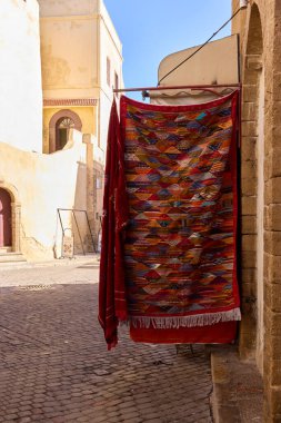 El 'Jadida' da dar bir caddenin karşısındaki parlak desenli tekstil perdeleri, güneşli taş binalara karşı canlı bir odak noktası oluşturuyor. Sahne 13 Haziran 2021 'de yerel kültürü yakalıyor.