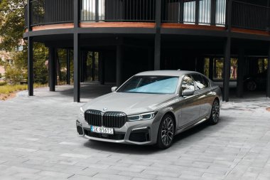 BMW 740D. Lüks bir sedan, verimli bir yeşillik ve modern mimari yapı ile çevrili, gösterişli, taştan bir garaj yolunda duruyor. Katowice, Polonya, 13.06.2021
