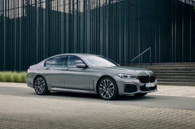 BMW 740D. Lüks bir sedan, çarpıcı modern binaların yanındaki asfalt bir alanda duruyor. Zarif çizgileri ve cilalı yüzeyi, Katowice, Polonya 13.06.2021 kentindeki gelişmişliği yansıtıyor.