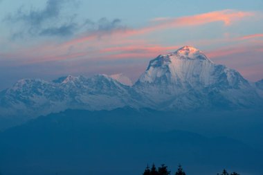 Dhaulagiri de dahil olmak üzere dağ sıraları gün doğumunda güneş ışığıyla parlar. Himalayalar 'daki Annapurna Ana Kampı' na giden bir yürüyüş rotasından görüldü..