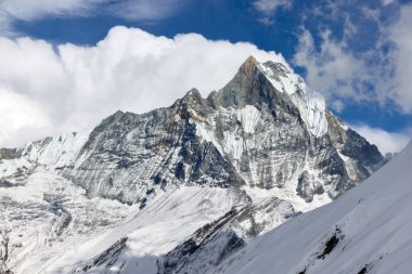 Nefes kesici bir manzara Machhapuchre Dağı 'nın gündüzleri Nepal' deki Annapurna Sığınağı 'nın karlı yamaçlarından yükseldiğini gösteriyor. Bulutlar mavi gökyüzünü dolduruyor