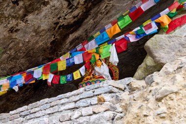 Bir Buda heykeli renkli Tibet dua bayraklarıyla süslenmiş kayalık bir oyuğa yerleştirilmiştir. Nepal 'deki bir gezi sırasında Annapurna Ana Kampı' na giden yolda.
