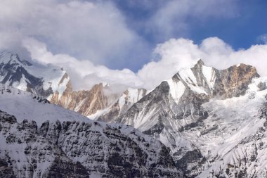 Karla kaplı zirveler görkemli bir şekilde gökyüzüne yükselir, bulutlar kısmen gizlidir. Himalayalar 'ın engebeli arazisi Annapurna Sığınağı, Nepal' de görülebilir..