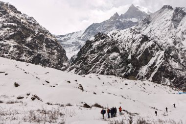 Gezginler Himalayalar 'da karla kaplı arazide yürürler. Nepal 'deki Annapurna Ana Kampı' na gidiyorlar. Arka planda görkemli dağlar beliriyor