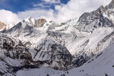 Himalayalar 'daki Annapurna Sığınağı' ndaki karla kaplı dağların manzarası. Manzara engebeli tepeleri ve kısmen bulutlu gökyüzünü gösteriyor..