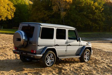 Gümüş renkli bir spor araç, bir Mercedes G-Class, kumlu zeminde duruyor. Araba yeşil ağaçların yanında. Güneş ışığı görülebilir. Sonbahardayız. Katowice, Polonya, 24.10.2015