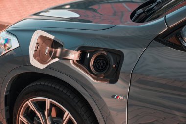 Gri bir BMW X1 eklenti hibrit elektrikli arabalar şarj portu tamamen açık, konnektörün elektriğe hazır olduğunu gösteriyor. Açık havada, gün ışığında. Katowice, Polonya, 07.30. 2021