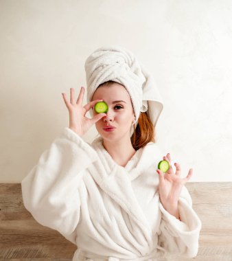 Bornozlu genç, güzel ev hanımı salatalıktan kozmetik bir maske yapıyor. 