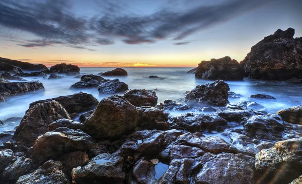 Sunrise on rocky shore and dramatic sky clouds — Stock Photo, Image