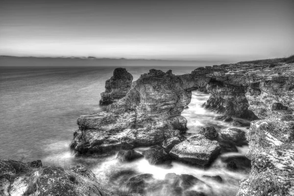 Beautiful sunrise over the sea and rocky shore on black and white — Stock Photo, Image