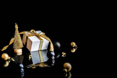 Hediye arka planı. Altın kurdeleli beyaz hediye kutusu, yeni yıl baloları ve tebrik kartı için siyah arka planda kış ağacı kompozisyonu. Metin için alanı olan Xmas arkaplanı